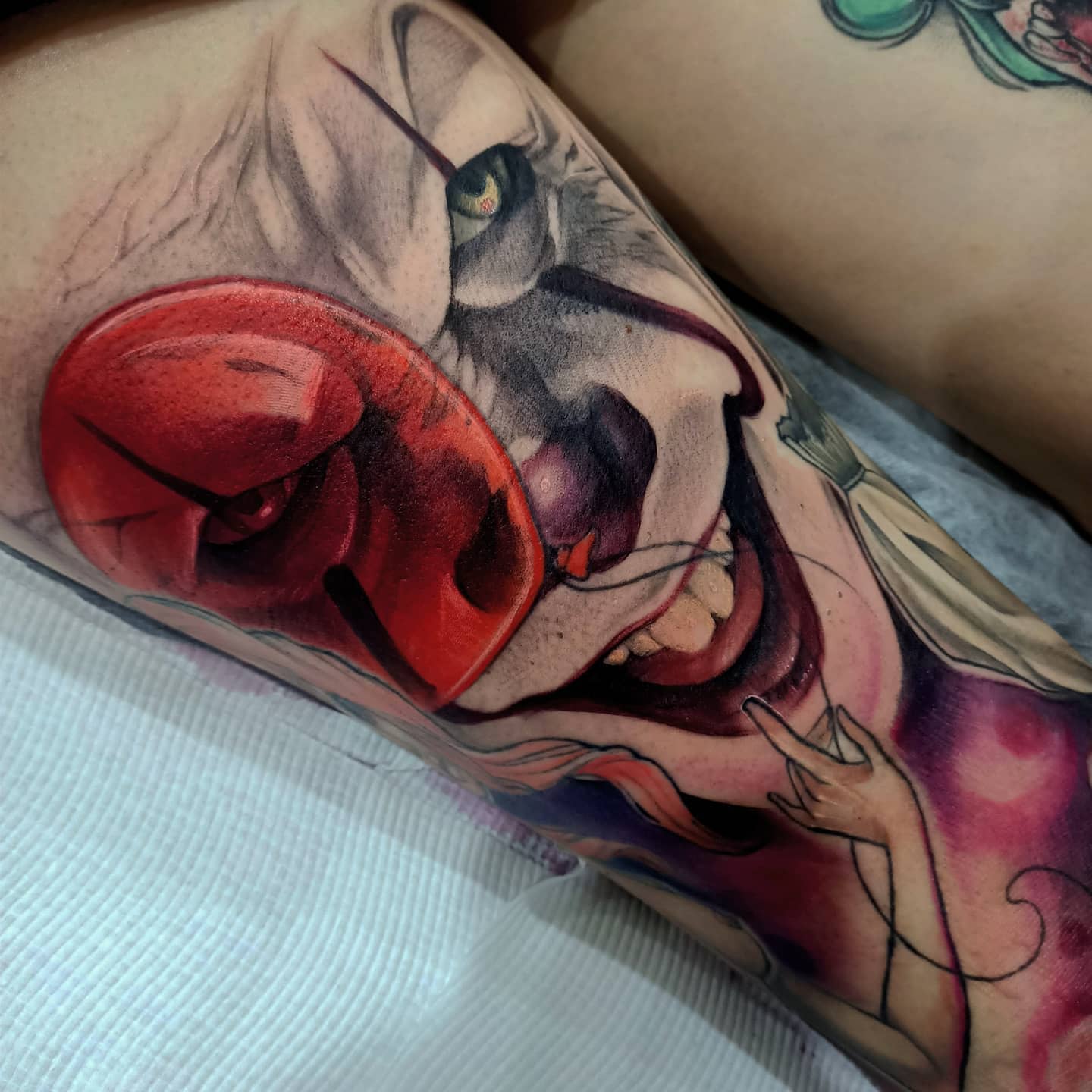Close-up Pennywise tattoo with a red balloon, capturing his sinister smile and piercing eyes